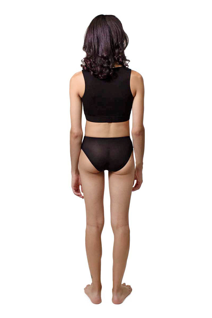 Mtf person wearing a black tucking underwear compression gaff with a cheeky boyshort cut and sheer back with a lycra bra, photographed from then back.