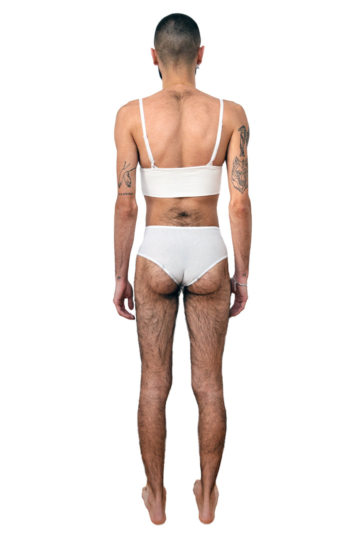 Non-binary person wearing a white tucking underwear compression gaff with a cheeky boyshort cut with a white bamboo bra, photographed from the back.