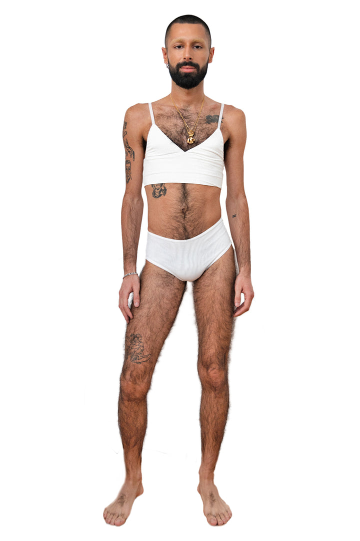 Non-binary person wearing a white tucking underwear compression gaff with a cheeky boyshort cut with a white bamboo bra, photographed from the front.