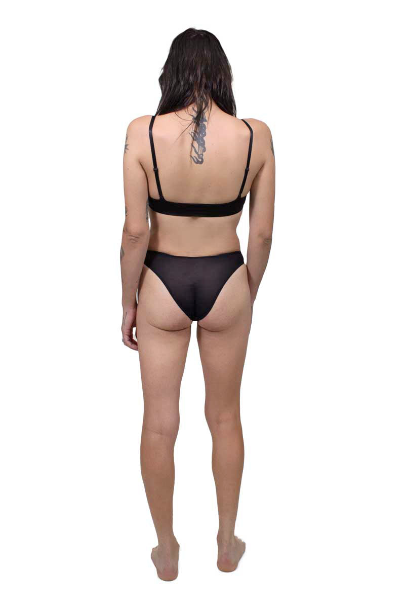 Mtf person wearing a black tucking underwear compression gaff with a cheeky cut and bamboo bralette, photographed from the back