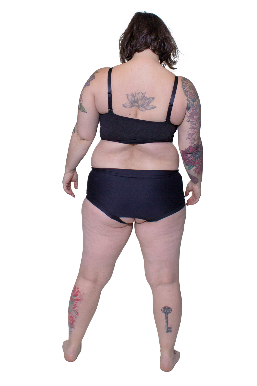 Plus-sized person wearing a black tank top chest binder made from breathable mesh with spaghetti straps, photographed from the back.