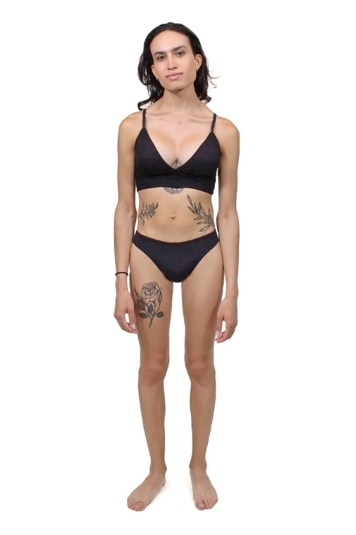 Mtf trans person wearing a black tucking underwear compression gaff with a cheeky cut, and a deep cut black bamboo bralette, photographed from the front.