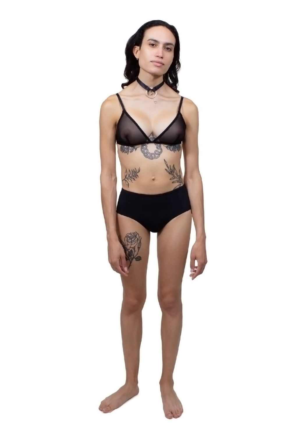 Transfemme person wearing a black tucking underwear compression gaff with a boyshort cut with a mesh bra, photographed from the front.