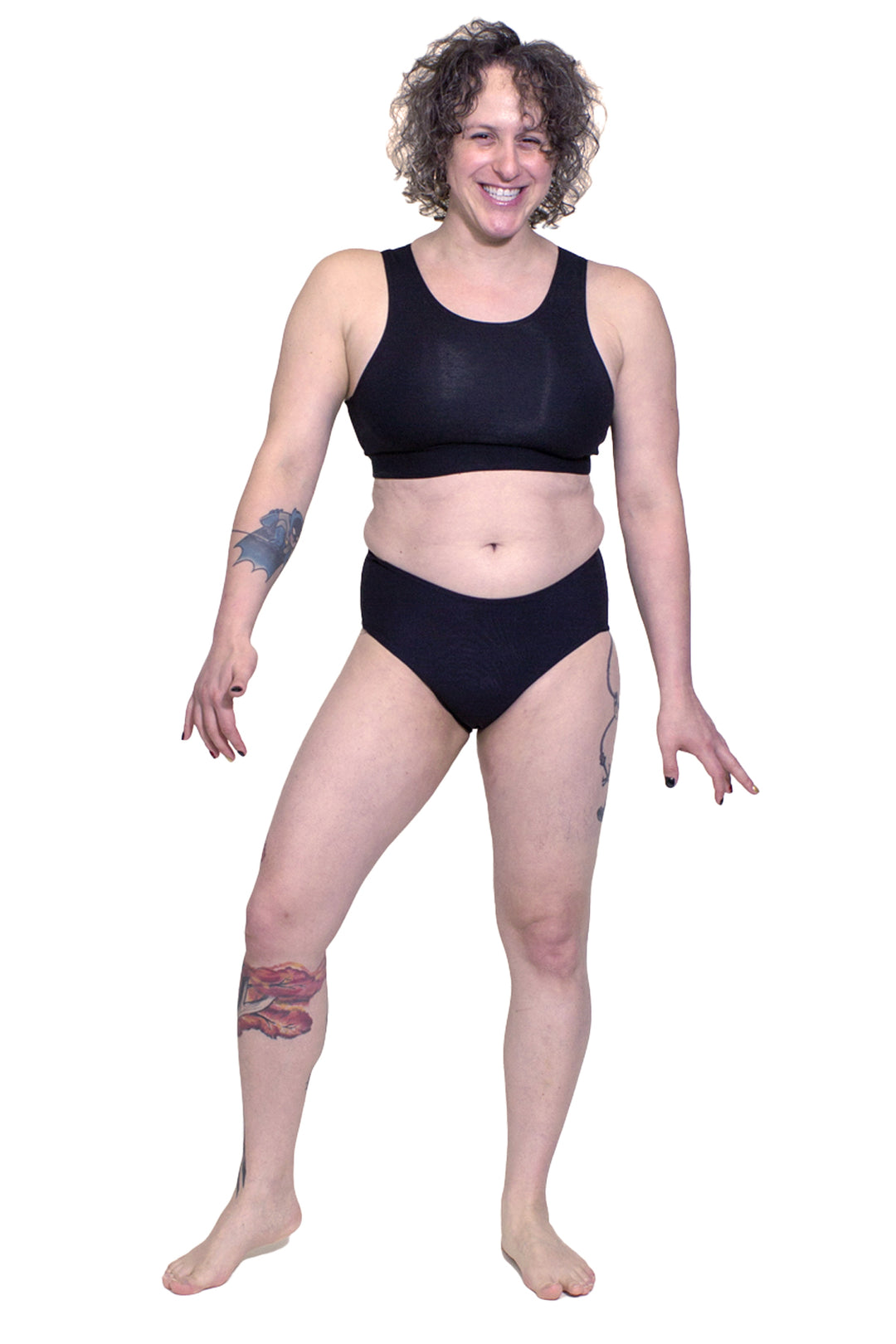 Transfemme person wearing a black tucking underwear compression gaff with a cheeky boyshort cut with a lycra bra, photographed from the front.