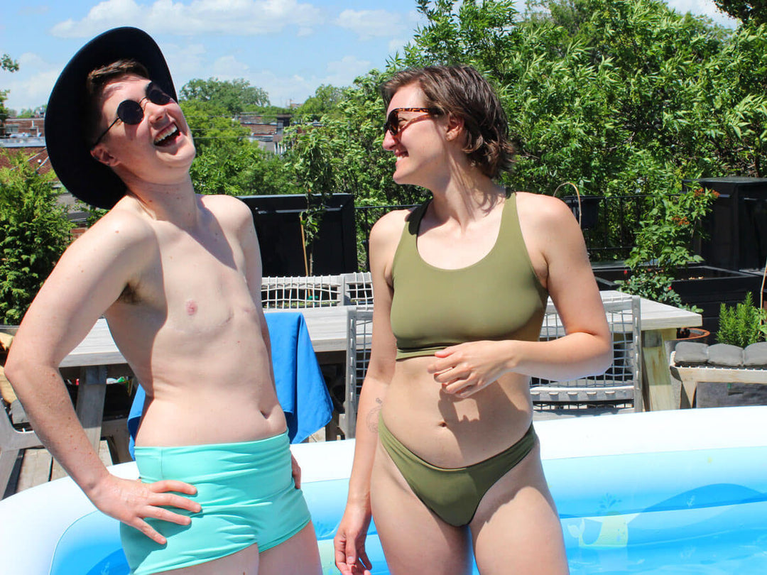 Two trans people in a pool in gender affirming swimwear.
