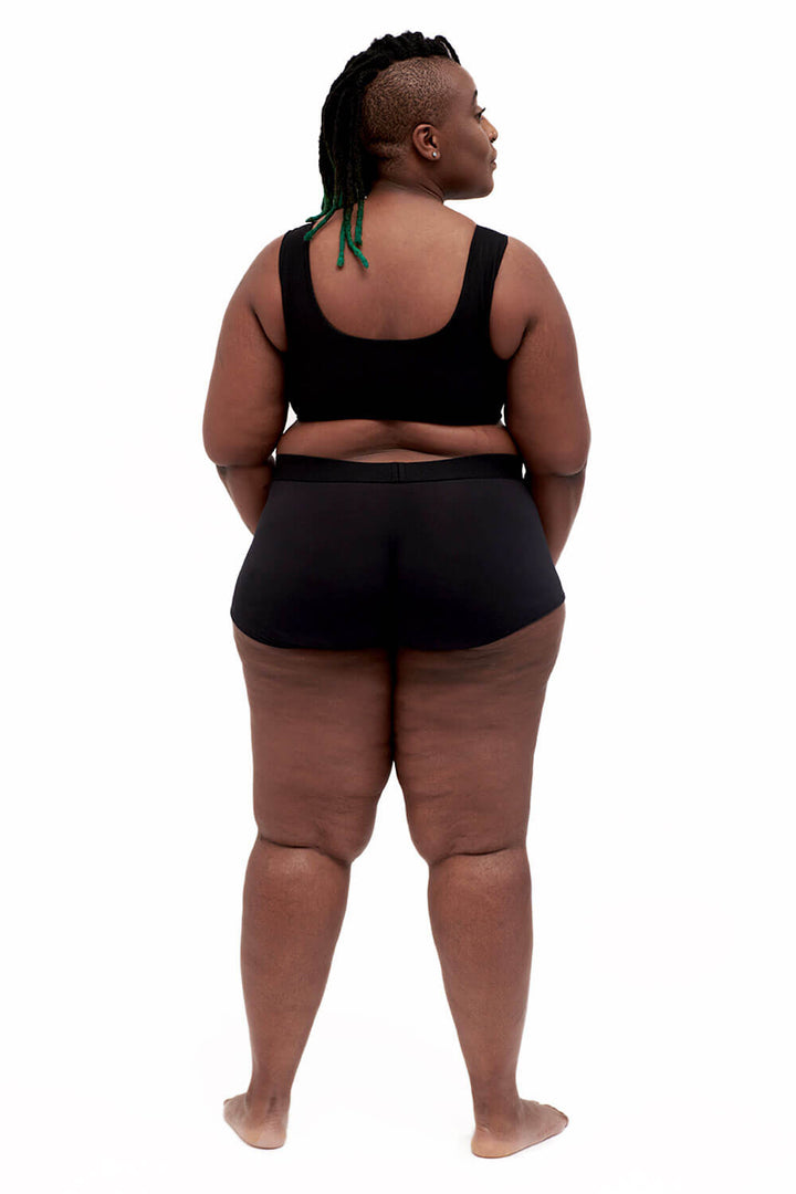Plus-sized person wearing a black sports bra style chest binder made from breathable mesh, photographed from the back.