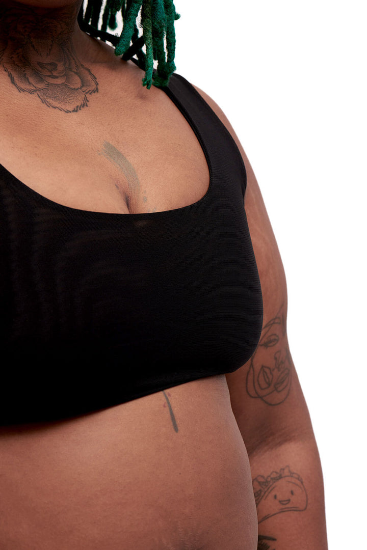 Detail of a plus-sized person wearing a black sports bra style chest binder made from breathable mesh, photographed from the front.