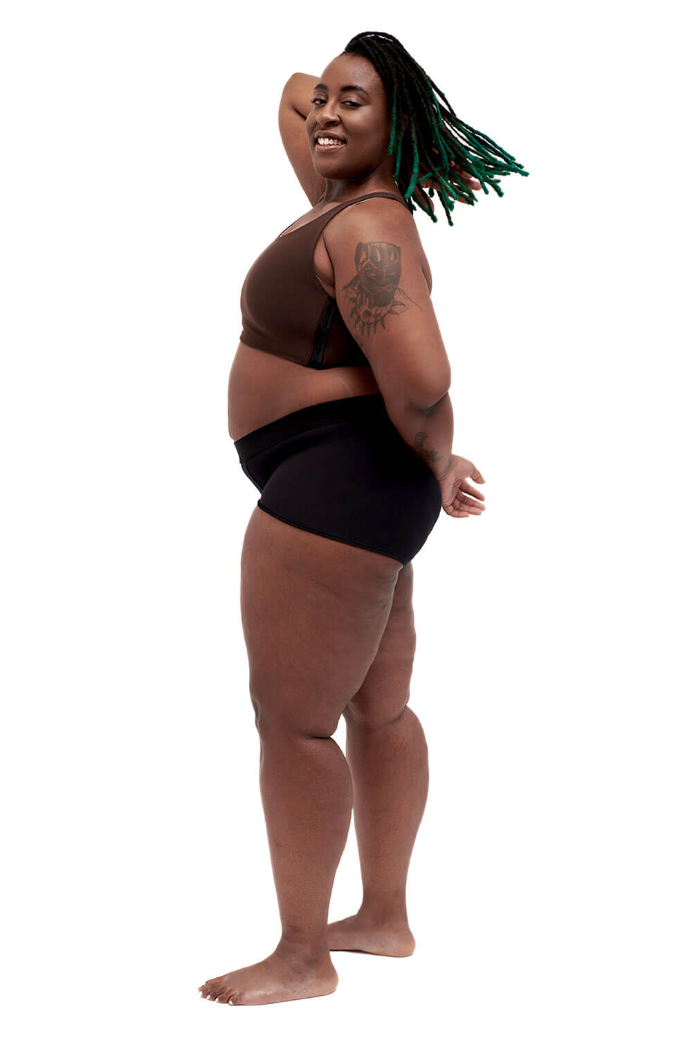Plus-sized person wearing a brown racerback side-open chest binder made from lycra, photographed from the side.