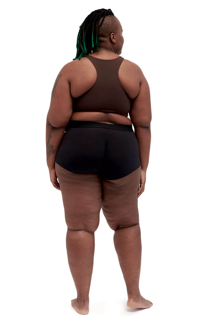 Plus-sized person wearing a brown racerback side-open chest binder made from lycra, photographed from the back.