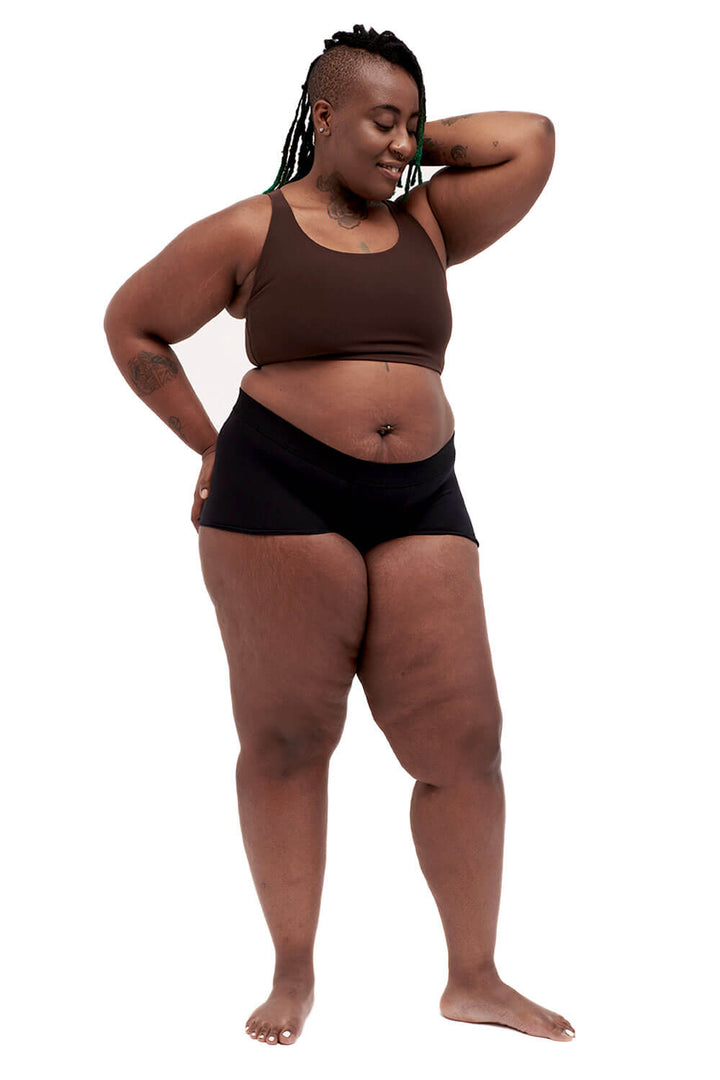 Plus-sized person wearing a brown racerback side-open chest binder made from lycra, photographed from the front, arms up.
