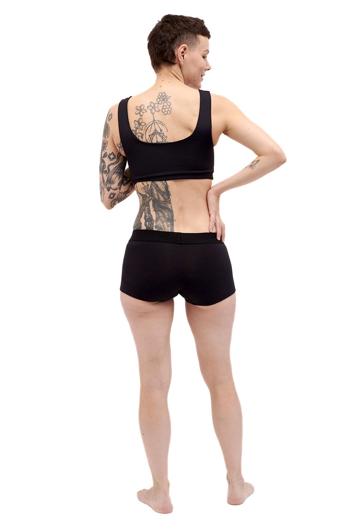 Petite person wearing a black sports bra chest binder made from lycra, photographed from the back.