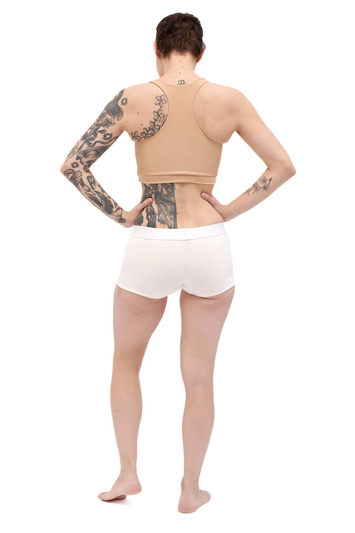 Petite person wearing a nude racerback chest binder made from lycra, shot from the back.