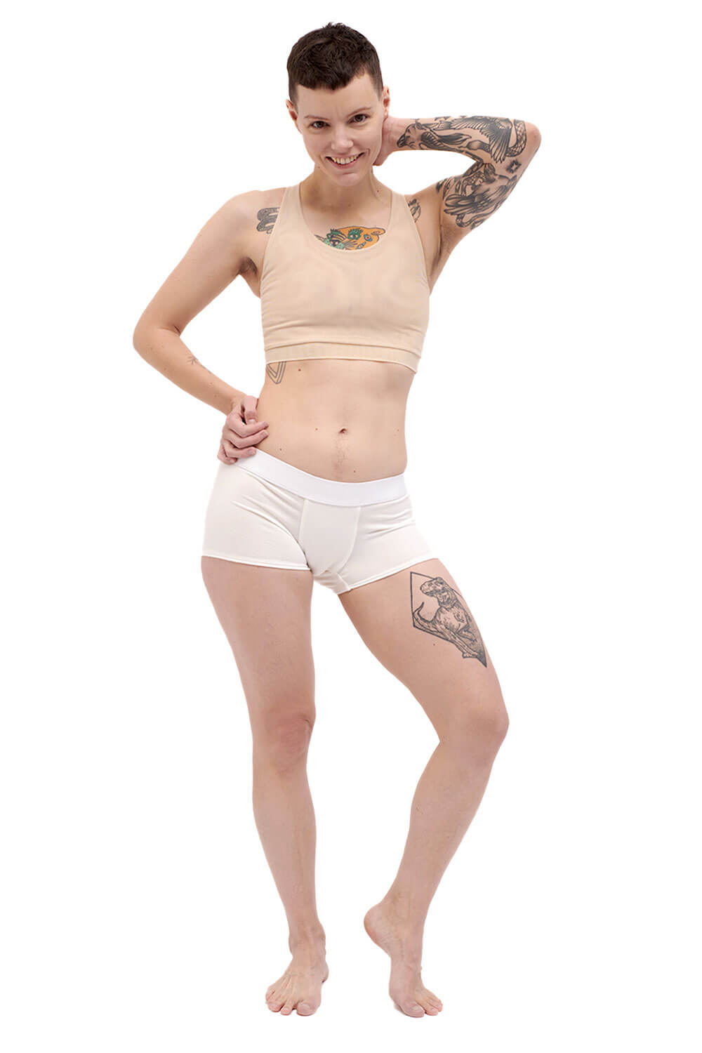 Petite person wearing a nude racerback chest binder made from mesh, photographed from the front with arms up.
