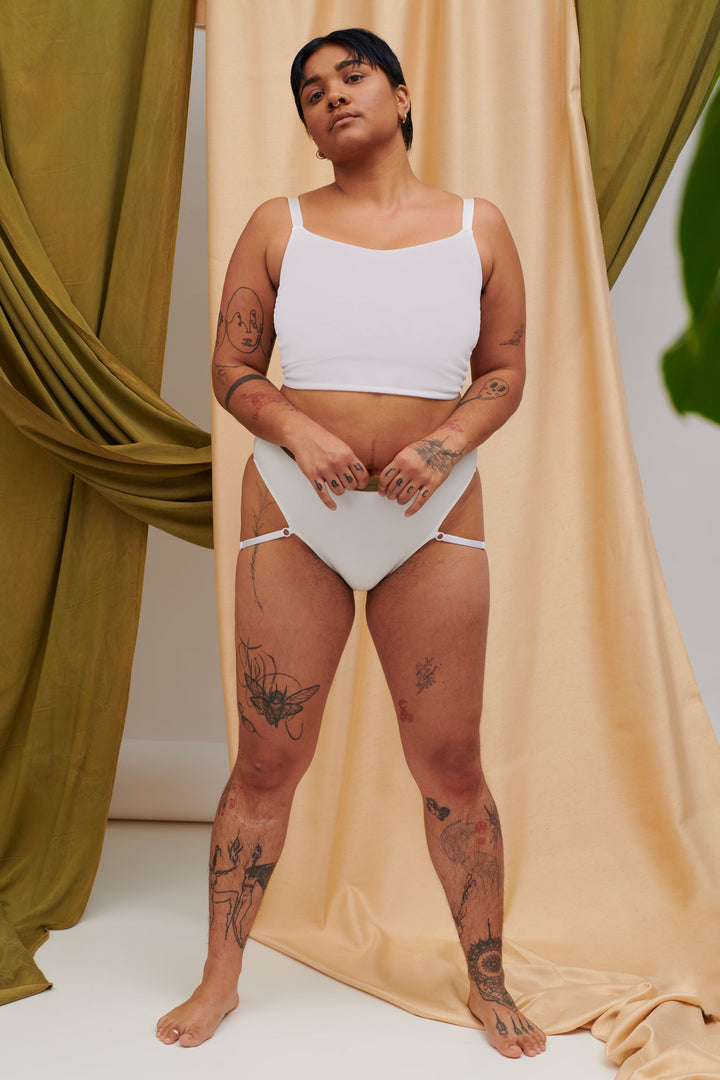 A Transgender Non-binary model look at the camera in the ortie sustainable collection mesh compression binder and ethical bamboo underwear. They look confident in their gender affirming chest binder