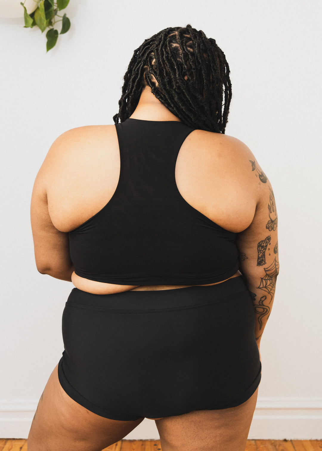 Plus-sized person wearing a black racerback soft chest binder made from lycra, photographed from the back.